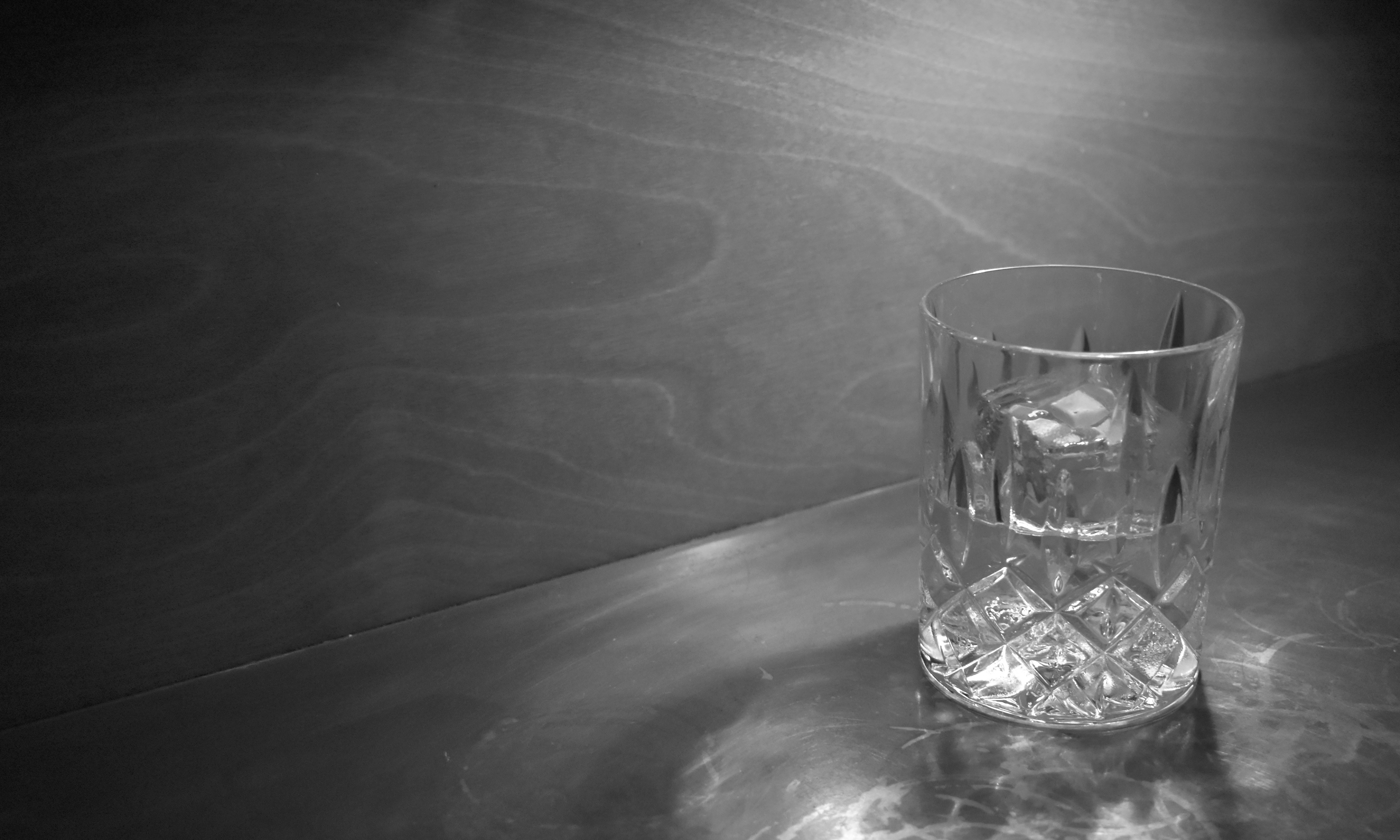 A lone drink on a shadowy bar top.